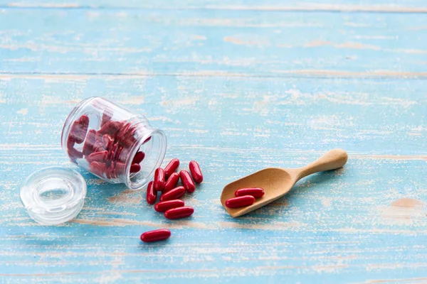 Tahta kaşık ve mavi masa üzerinde cam şişelerde kırmızı ilaçlar. Farmasötik ilaç veya vitamin hapları, tabletler ve kapsüller