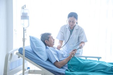 Banknot ile Asyalı kadın profesyonel doktor gülümseyerek konuşma ve hastane koğuşunda hasta yatağında yatan yaşlı adam hasta teşhis