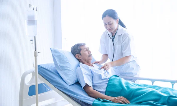 Banknot ile Asyalı kadın profesyonel doktor gülümseyerek konuşma ve hastane koğuşunda hasta yatağında yatan yaşlı adam hasta teşhis
