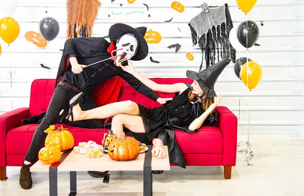 Feliz concepto de fiesta de Halloween. Joven hombre y mujer vistiendo la fantasía como vampiros, brujas o fantasmas celebran el festival de Halloween en la habitación decorada con globo, murciélago y calabaza . — Foto de Stock