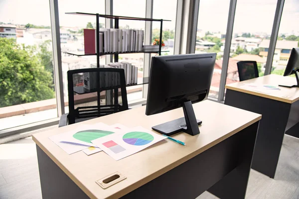 Moderne Büroeinrichtung mit Tisch, Computer, Monitor, Bericht und großem Glasfenster im Raum ohne Menschen — Stockfoto