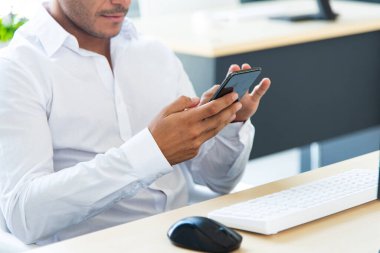 Kendine güvenen genç yönetici, yönetici, bilgisayarla çalışıyor ve modern ve yaratıcı ofiste akıllı telefon kullanıyor. Sosyal uzaklık durumunda çalışmak
