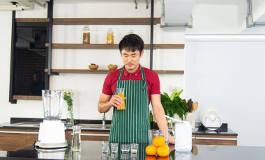 Akıllı ve yakışıklı Asyalı adam tavan arası mutfağında sağlıklı yemek ve portakal suyu hazırlıyor..