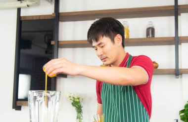 Akıllı ve yakışıklı Asyalı adam, tavan arası mutfağında sağlıklı yemek ve taze organik portakal suyu hazırlıyor..