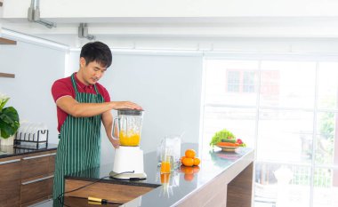 Akıllı ve yakışıklı Asyalı adam, tavan arası mutfağında sağlıklı yemek ve taze organik portakal suyu hazırlıyor..