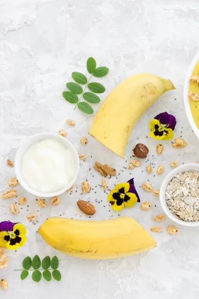 Ingredients for smoothie: banana, yogurt, nuts, oatmeal, Chia seeds, air wheat on concrete background. Overhead food shots. Healthy food, Clean Eating or Vegetarian concept.