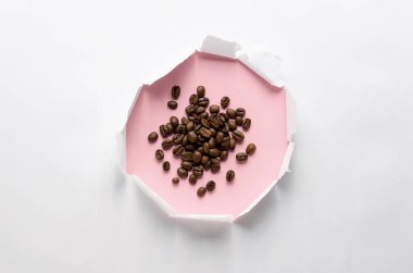 Pembe arka plan üzerinde beyaz kağıt ve kahve çekirdekleri kağıt delik.