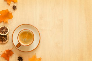 Bir fincan kahve ve sonbahar yaprakları ahşap arka planda.