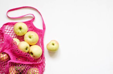 Beyaz ahşap zemin üzerinde taze elmalar bulunan pembe ağ alışveriş torbası.