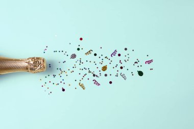 Mavi masa arkasında altın konfeti yıldızları olan şampanya şişesi. Parti konsepti.