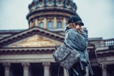 Saint Petersburg, Rusya - 10.18.2019: Sıcak giysili ve eşarplı kız Kazan Katedrali 'nin arka planında kameraya döndü.