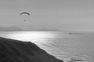 Sahildeki uçurumlarda yamaç paraşütü pratiği yapan biri. Siyah beyaz fotoğraf.