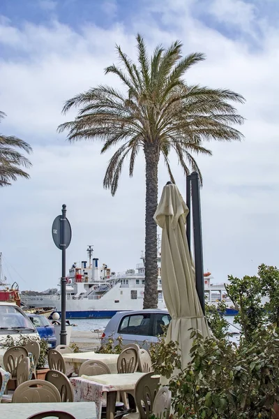 Traghetto in porto attraverso tavolini da caffè all'aperto con palma — Foto Stock