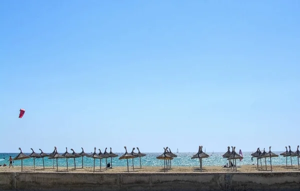 Песчаный пляж с зонтиками, огромным голубым небом и кайтсерфингистами — стоковое фото