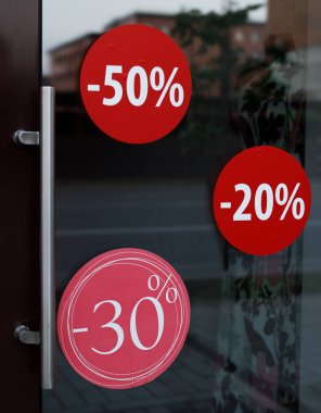 Perakende satış mağazasının girişinde büyük bir kırmızı satış afişi var. Mağazanın girişinde indirim etiketleri var. Yüzde 50 'ye kadar satılıyor. Mevsimlik Satış
