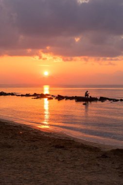 Denizde gün batımında adam balık yakalar.