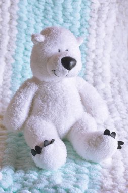 Beyaz oyuncak ayı örgü örülmüş hafif bir battaniyenin üstünde.