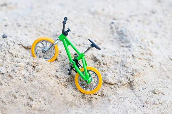 a bike with a green frame and yellow wheels, standing on the sand, a small copy of the bike to perform tricks