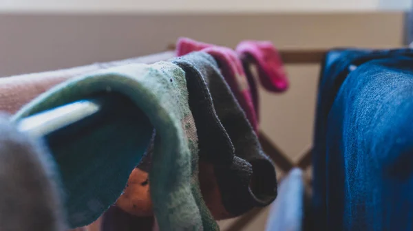 Visão escura, filtrada e desbotada de pares de meias incompatíveis secando em um rack de lavanderia, pendurado para secar após a lavagem, com jeans azul mostrando e foco seletivo. Representando dia de lavanderia, tarefas, limpeza, falta de meias, etc . — Fotografia de Stock