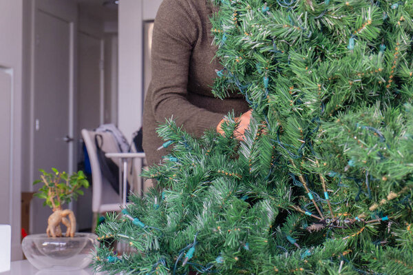 Woman behind an artificial Christmas tree, setting up the holiday decoration by unravelling branches