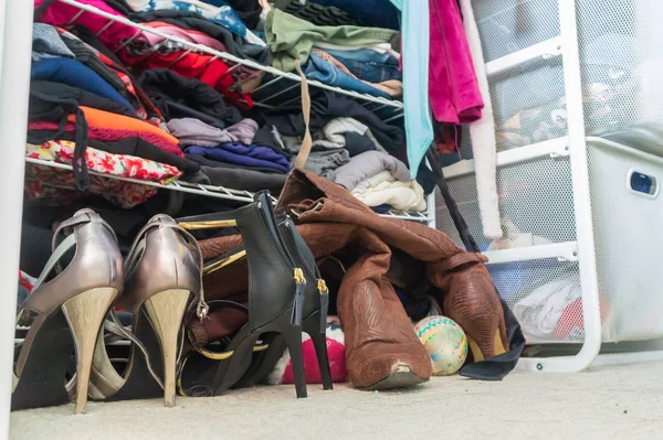 Armario de mujer con zapatos de tacón alto, apilados, ropa doblada en estantes y parte de batas colgadas. Representación de la organización del armario, tiempo para donar ropa, estilo de vida de moda, consumismo, etc. . — Foto de Stock