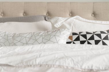 Gri, beyaz, siyah, altın ve beyaz yatak dekoratif yatak yastıkları. Arka planda Bej kumaş tufted başlık. Kabarık ve rahat görünümlü yatak yakın çekim.
