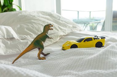 Toy dinosaur and car on parent's bed, depicting family home and parenting life. White linens in background. clipart