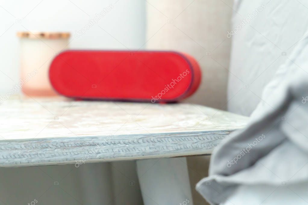 Bright red radio alarm clock and candle jar on a bedside table nightstand, with bed and linens showing in soft colors.