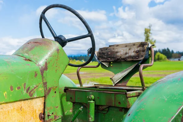 Egy farmon régi, törött traktorülés. Mutatja a kerék és a fa támogatását. Zöld és sárgás öreg mezőgazdasági gépek. — Stock Fotó