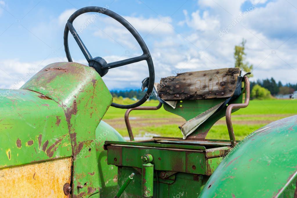 Old broken tractor seat on a farm. Shows the wheel and wood backing. Green and yellow old farm equipment.