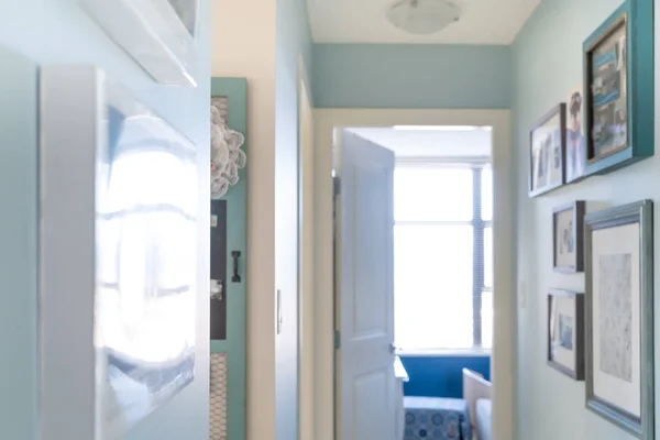 Home apartment hallway with picture frames as wall art, for interior decor with matching blue design and painter's work. Scene is a little hazy and bright.