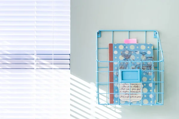 Wall hanging wire basket holding a notebook in a bright home office, next to a window, on a mint green painted wall. — Stock Photo, Image