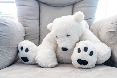 Beyaz oyuncak ayı oyuncak bir peluş gri çocuk sandalyesi üzerinde kambur. Doğal güneş ışığı ile arkadan aydınlatmalı.
