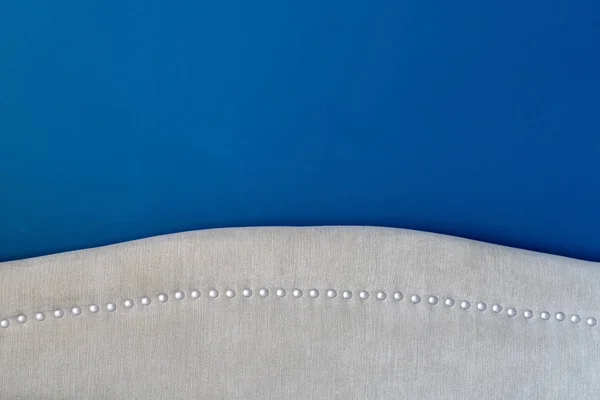Deep royal blue painted wall with an upholstered headboard close up, showing the silver nail heads and beige fabric detail. Matching interior decor. — Stock Photo, Image