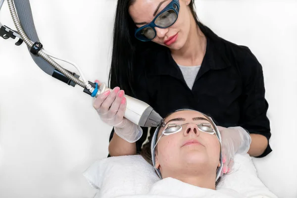 Estetista che utilizza un laser cosmetico sul viso di una donna per il ringiovanimento del viso per levigare la pelle, su uno sfondo bianco in una spa medica . — Foto Stock