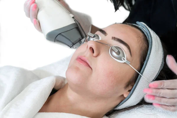 Primo piano del manipolo laser utilizzato per il ringiovanimento della pelle sul viso della donna, con le mani del tecnico di bellezza che tengono apparecchiature laser in una spa medica. Fondo bianco . — Foto Stock