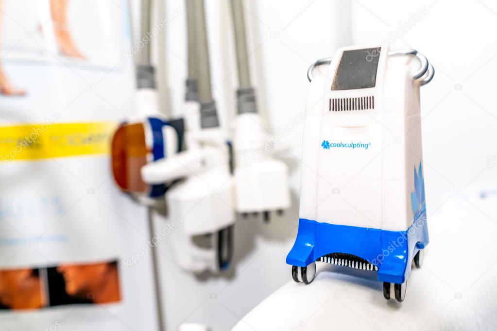 Miniature Coolsculpting machine model in a medspa clinic, on a patient bed in a branded room for cryolipolysis treatment to remove fat.