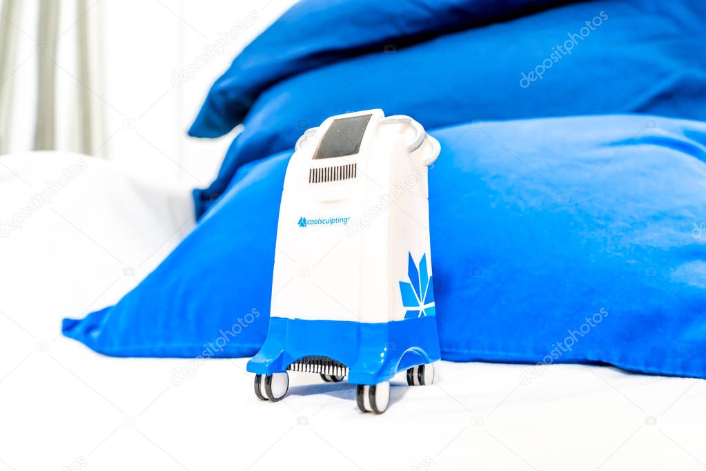 Miniature Coolsculpting machine model in a medspa clinic, on a patient bed in a branded room for cryolipolysis treatment to remove fat.