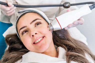 Bir güzellik cilt sıkma tedavisi sırasında bir kadının yüzünün yanak üzerinde radyo frekansı microneedling makine el parçası.