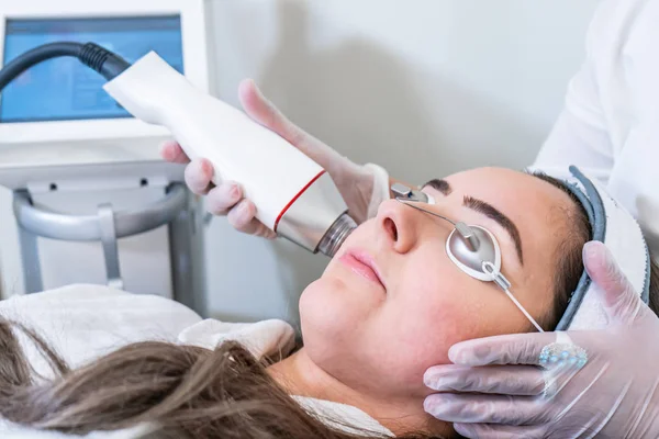 Beautician applying radio frequency microneedling handpiece to a woman's face for skin tightening treatments at a beauty clinic. — Stock Photo, Image