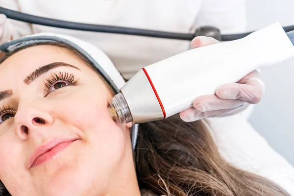 Bir güzellik cilt sıkma tedavisi sırasında bir kadının yüzünün yanak üzerinde radyo frekansı microneedling makine el parçası.