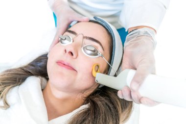 A 532 ve 1064 nm dalga boyu ve Nd:Yag lazer bir güzellik kliniğinde, kadın hasta üzerinde bir cilt tedavisi olarak kullanılmaktadır. Cilt üzerinde lazer doğrudan dairesel halka ile el parçası gösterir. Gözlük takan hasta.