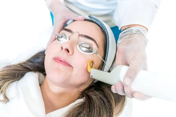 A 532 and 1064 nm wavelength and Nd:YAG laser being used as a skin treatment on female patient, in a beauty clinic. Shows hand piece with circular ring to direct laser on skin. Patient wearing goggles. — Stock Photo, Image