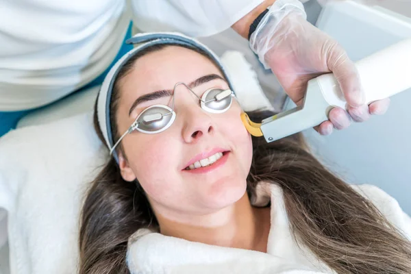 A 532 and 1064 nm wavelength and Nd:YAG laser being used as a skin treatment on female patient, in a beauty clinic. Shows hand piece with circular ring to direct laser on skin. — Stock Photo, Image
