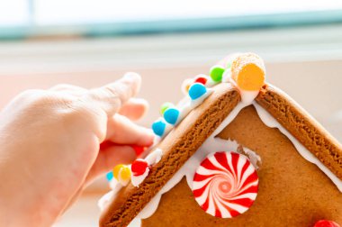 Yaratıcı ve klasik, mevsimlik tatil etkinliği olarak pudra şekeri ile zencefilli evin çatısına şeker topları ve gummies yerleştirerek çocuk parmakları.