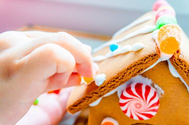 Yaratıcı ve klasik, mevsimlik tatil etkinliği olarak pudra şekeri ile zencefilli evin çatısına şeker topları ve gummies yerleştirerek çocuk parmakları.