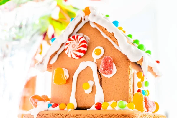 Cute, child-made gingerbread house, with imperfections (a real gingerbread house assembly), for the Christmas holiday season, as a decoration. Classic holiday activity and dessert.