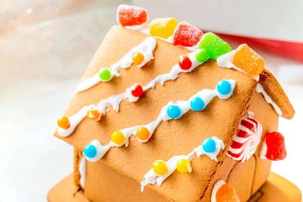 Cute, child-made gingerbread house, with imperfections (a real gingerbread house assembly), for the Christmas holiday season, as a decoration. Classic holiday activity and dessert.