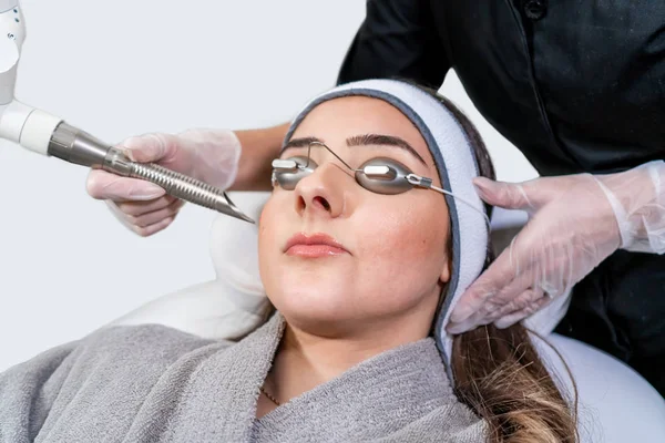 Специалист по лазерной лазерной терапии красоты проводит сеанс косметической обработки кожи на пациентке, также называемой лазерной кожурой или фотолицевой, с помощью лазера Er: Yag (инфракрасная длина волны ). — стоковое фото