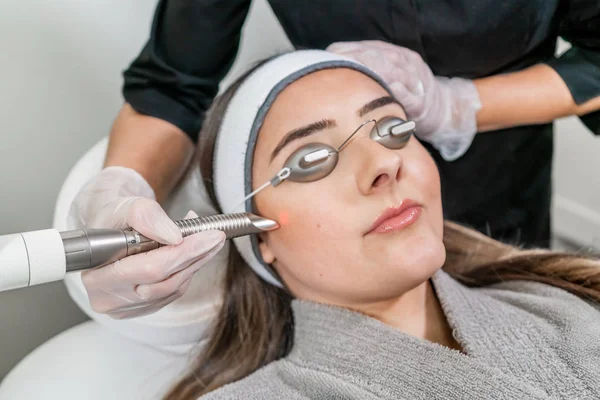 Beauty laser technician performing a cosmetic skin resurfacing session on a female patient, also called a laser peel  or photofacial, with an Er:Yag laser (infrared wavelength). — Stock Photo, Image
